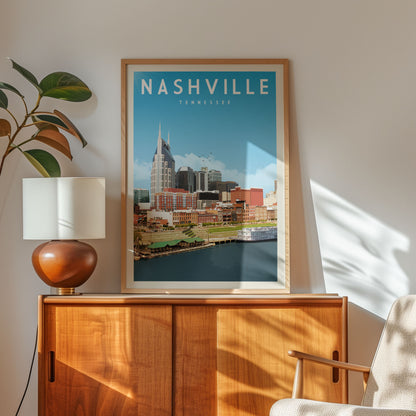 A framed poster of Nashville, Tennessee, featuring a cityscape with a river and buildings, is displayed on a wooden cabinet in a room with a lamp and a plant.