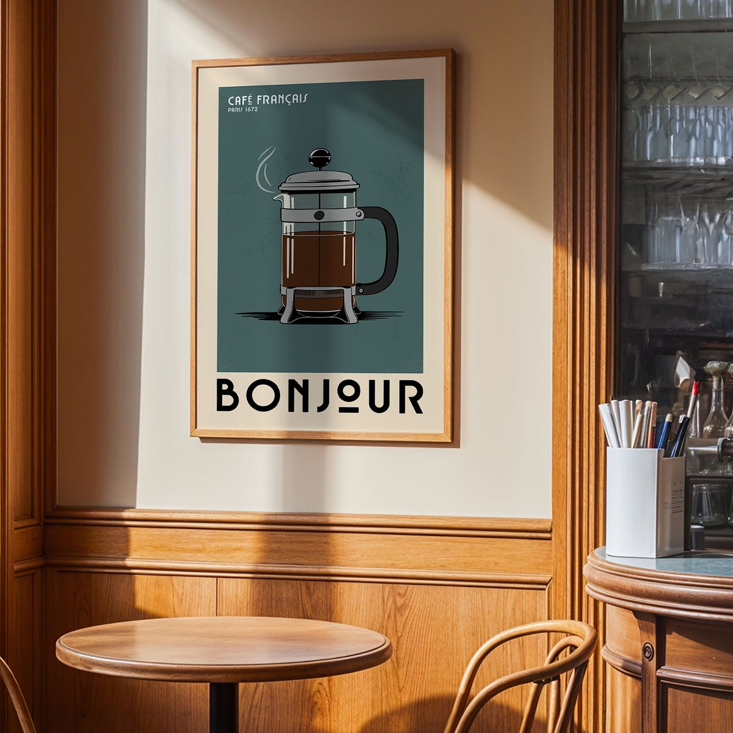a framed poster of a French press coffee maker hanging on a wall, with a wooden table and chairs in the foreground.