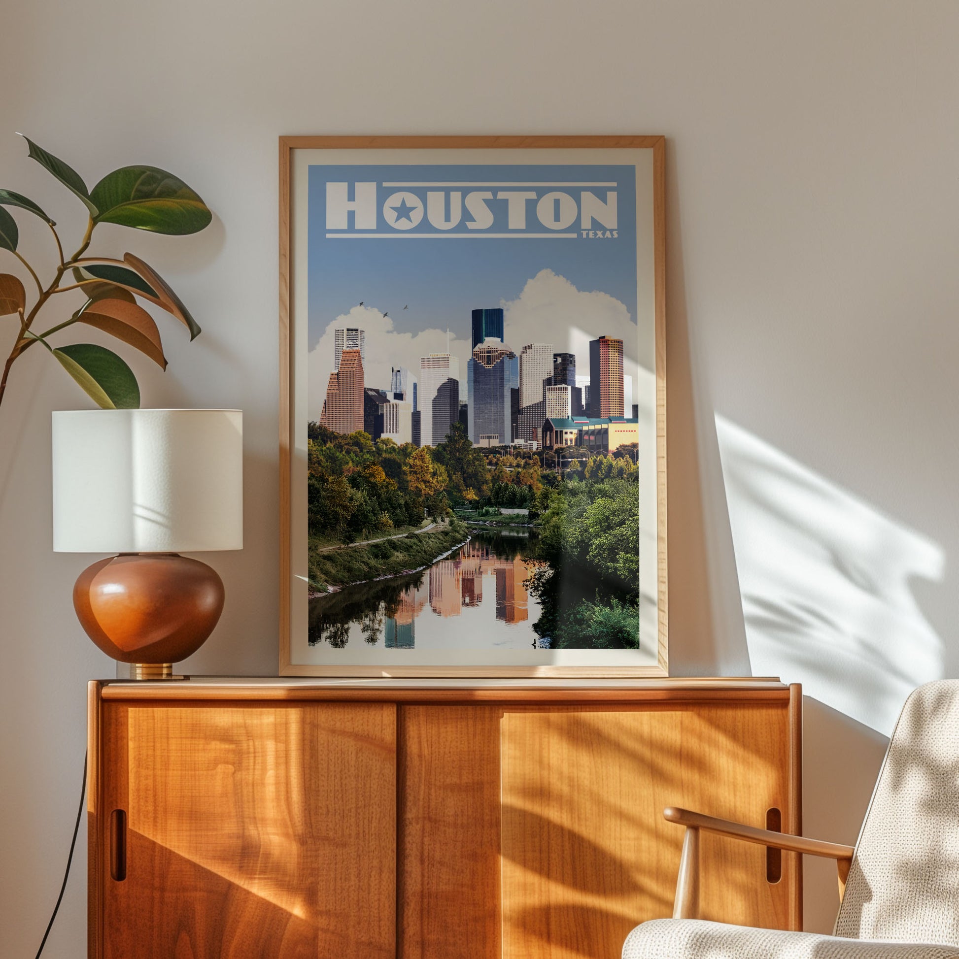 a framed poster of the Houston skyline, with a wooden cabinet and a lamp in the foreground.