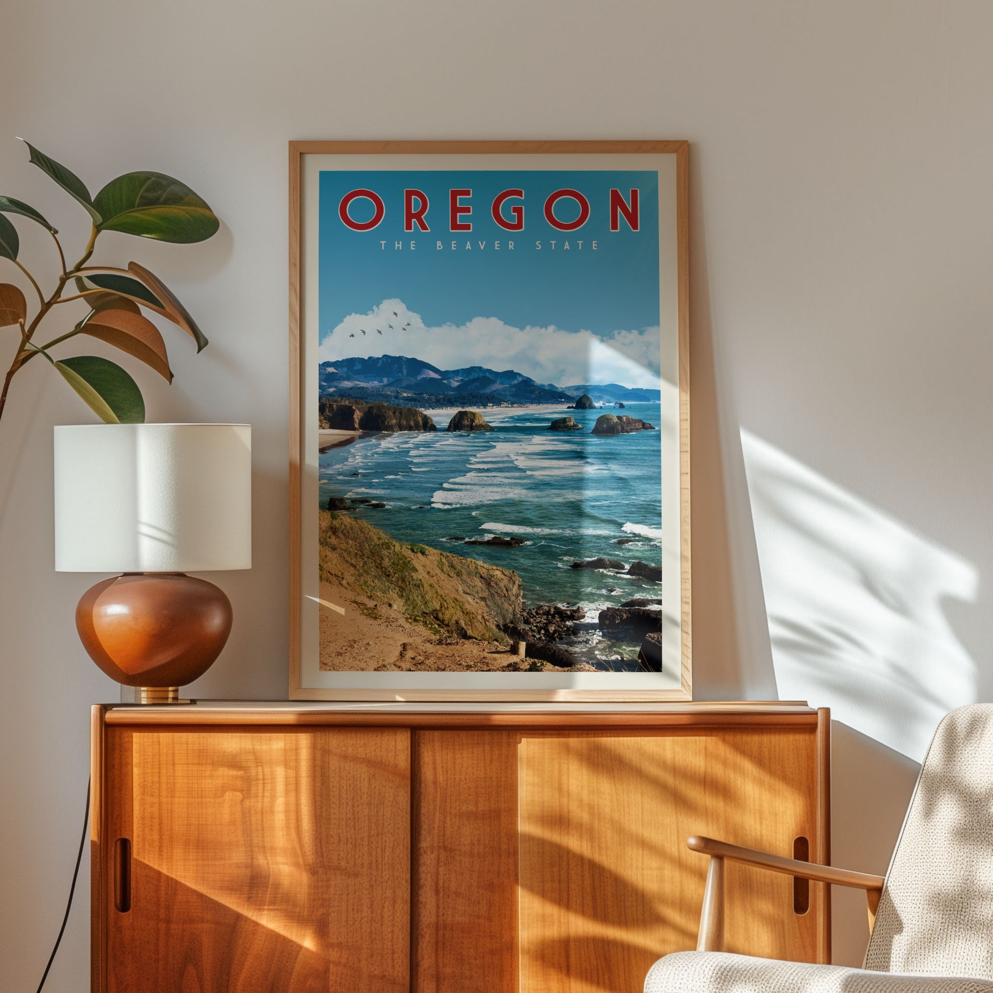 a framed poster of a scenic coastal landscape with mountains and the ocean, hanging on a wall next to a wooden cabinet and a lamp.