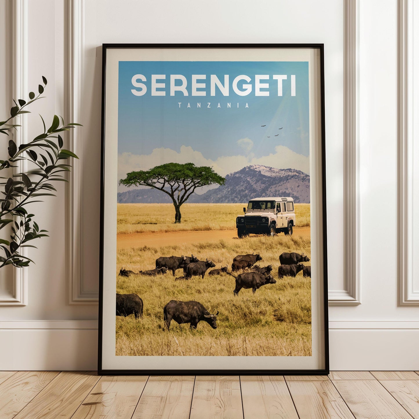 The image is a framed poster of a safari scene in Tanzania, featuring a herd of wildebeest grazing in the foreground and a safari vehicle in the background.