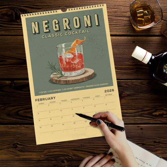 A person is writing in a notebook while holding a pen, with a calendar for "Negroni Classic Cocktail" displayed on a wooden table.